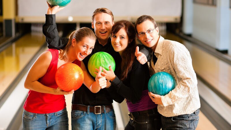 Vier Freunde mit Bowlingkugeln, lachen in Kamera