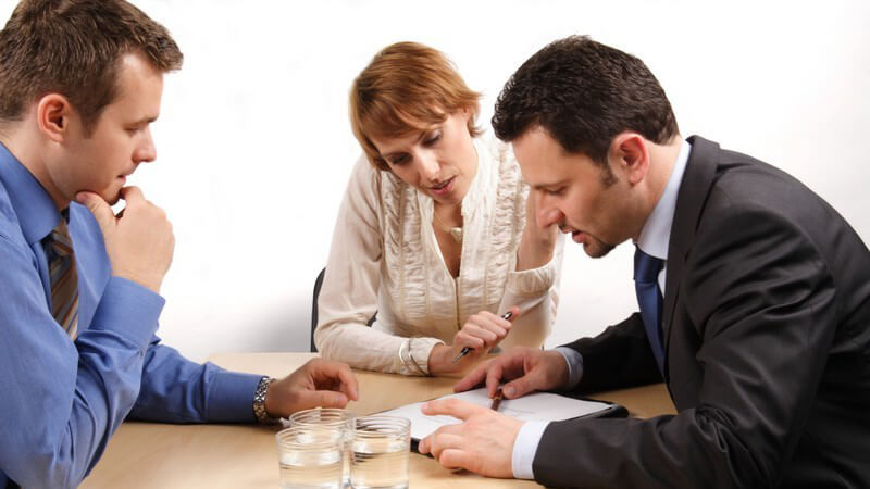 Drei Geschäftsleute sitzen am Tisch und besprechen einen Vertrag