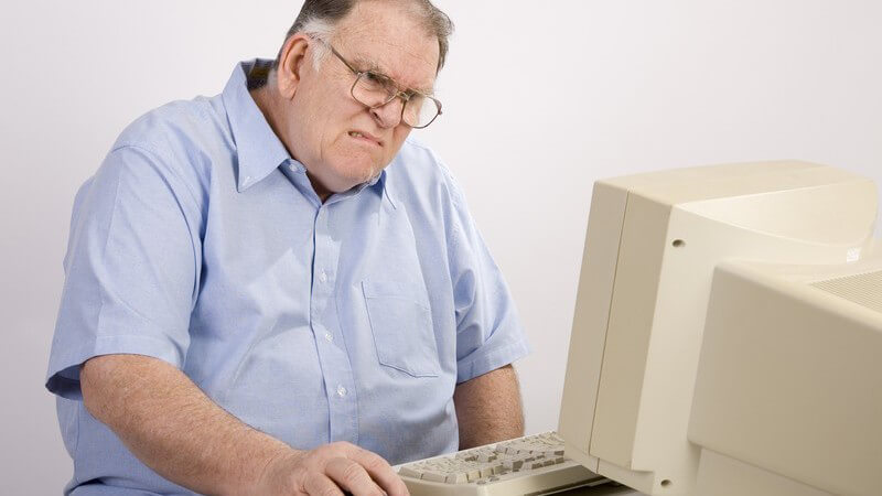 Älterer Mann sitzt vor Computer und macht mürrisches Gesicht