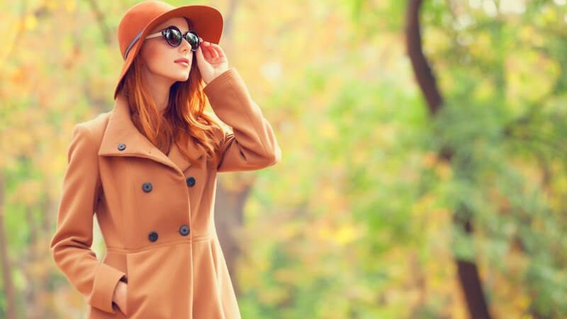 Herbst - Frau mit Mantel, Hut und Sonnenbrille macht Spaziergang im Park