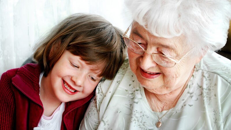 Großmutter mit Brille, links junge Enkelin in rotem Pullover