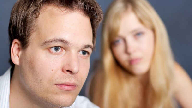 Vorne dunkelhaariger junger Mann in Hemd mit traurigem Blick, hinten blonde junge Frau mit erwartungsvollem Blick