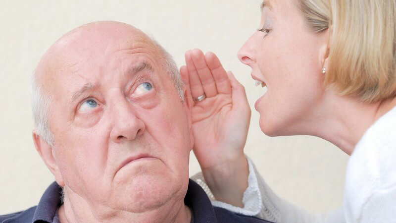 Ältere Frau sagt ihrem schwerhörigen Mann etwas ins Ohr