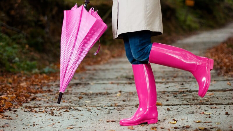 Herbst, Unterkörper einer Frau mit pinken Gummistiefeln und Regenschirm