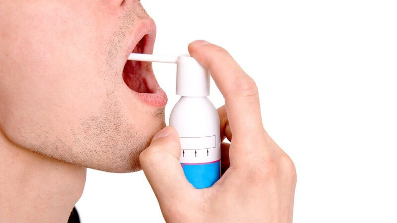 Hand hält Asthmaspray vor offenen Mund, weißer Hintergrund