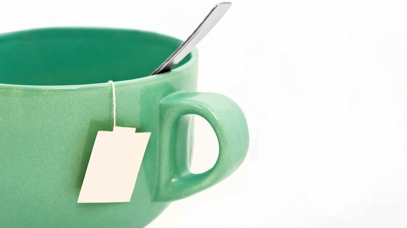 Löffel und Teebeutel in grüner Tasse auf weißem Hintergrund