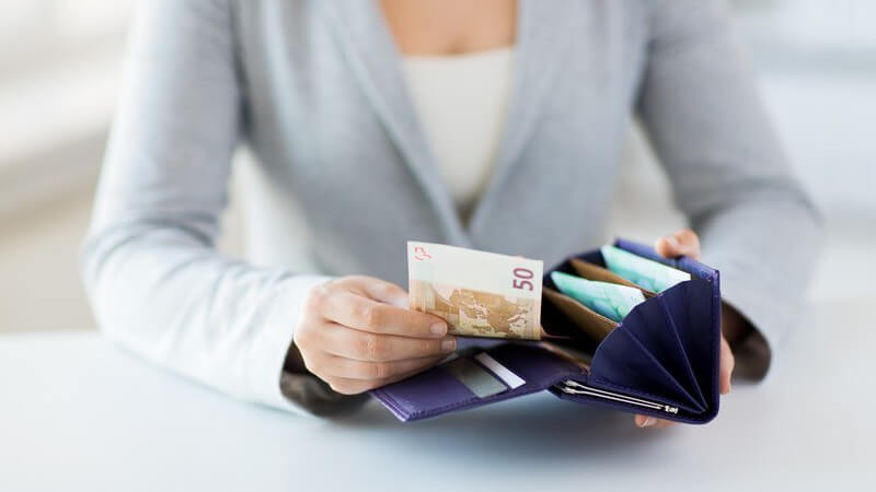 Frau in grauer Strickjacke sitzt am Tisch und nimmt einen 50-Euro-Schein aus der Geldbörse