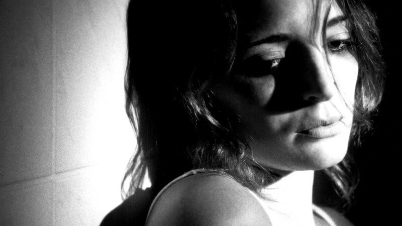 Schwarz-weiß Bild junge Frau lehnt an Wand, trauriges Gesicht, Drogensucht