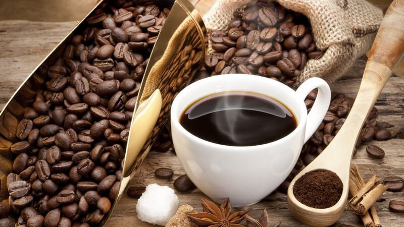 Tasse Kaffee, daneben gemahlener Kaffe sowie ganze Kaffeebohnen