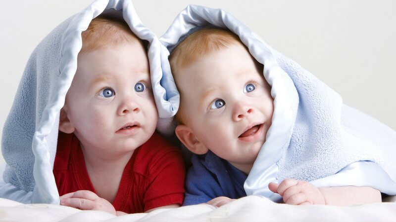 Zwillinge mit Decke über dem Kopf schauen neugierig zur Seite