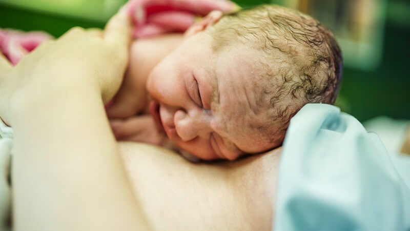Neugeborenes liegt kurz nach der Geburt in rosa Decke auf dem Körper der Mutter