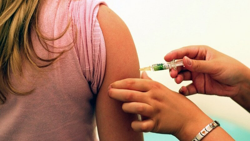 Rechter Oberarm einer jungen Frau wird von einer Krankenschwester mit Nadel geimpft, Ansicht von hinten