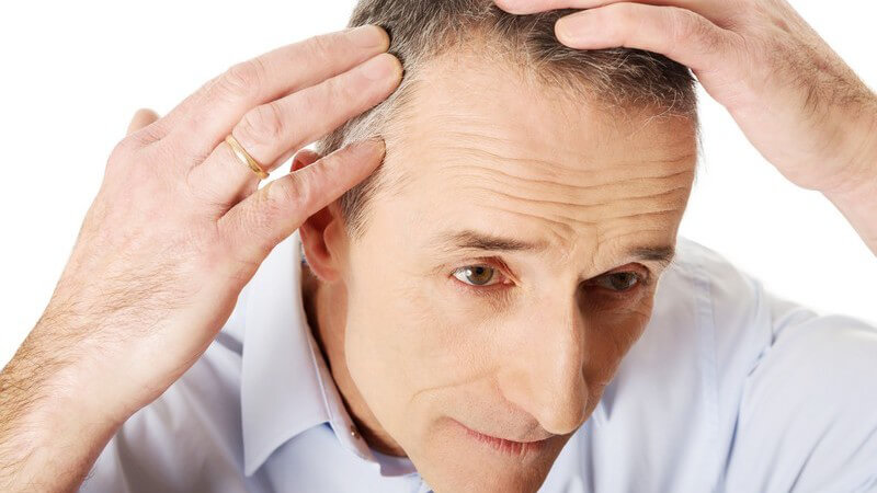 Älterer Mann in Hemd untersucht seine leicht ergrauten Haare