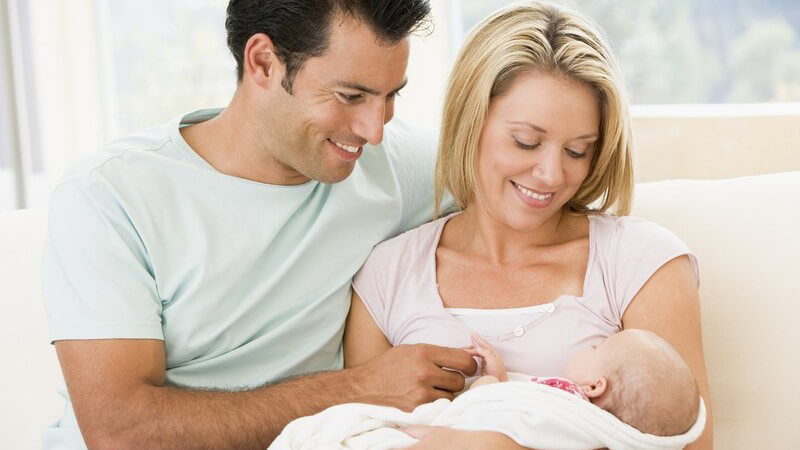 Junge Eltern mit Neugeborenem auf Couch