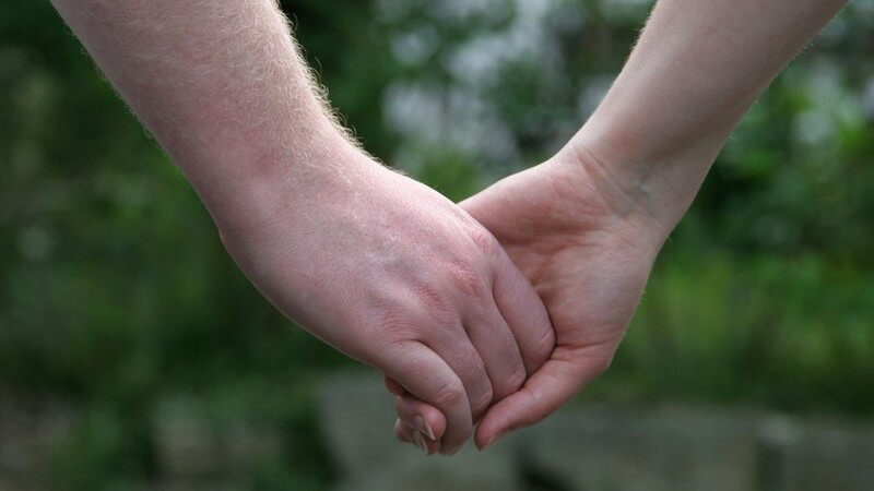 Eine Männer- und eine Frauenhand greifen ineinander, vor grünem Pflanzenhintergrund