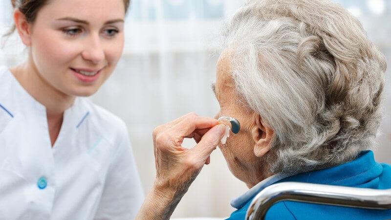Junge Krankenschwester und alte Frau mit einem Hörgerät im Ohr