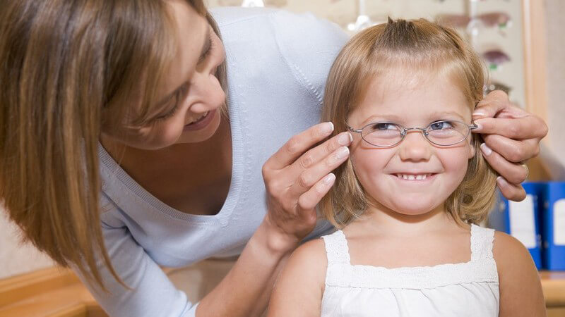 Mutter setzt ihrer kleinen Tochter beim Optiker Brille auf