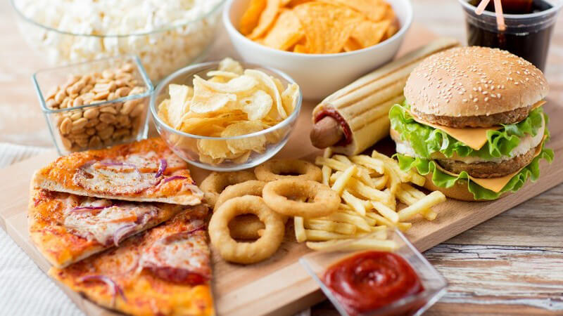 Diverse Fast Food-Speisen auf Holzbrett - Pizza, Burger, Pommes, Chips und Cola