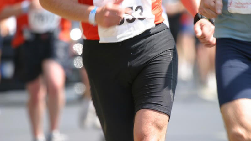 Unterleibe, Beine und Startnummern von Marathonläufern auf der Straße bei Sonne