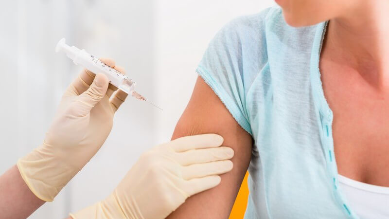 Frau in blauem Shirt bekommt eine Spritze mit Impfstoff in den rechten Oberarm