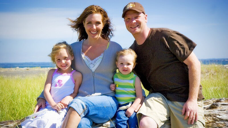 Familie von glücklicher Familie, Mutter, Vater, Kleinkinder (Mädchen und Junge) auf Baumstamm auf Düne vor Strand