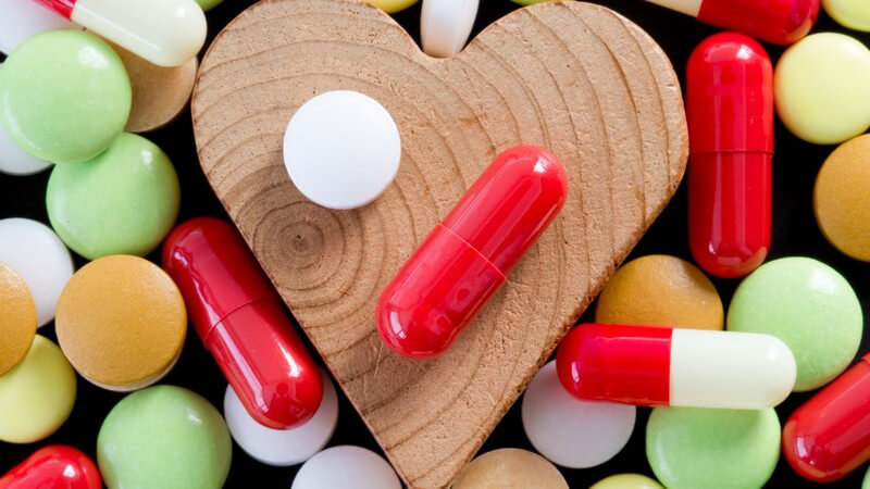 Bunte Pillen und Kapseln umringen ein Herz aus Holz