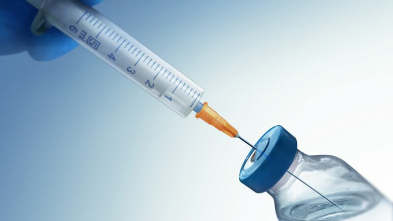 Spritze zieht Wirkstoff, Impfstoff aus Glasfläschchen