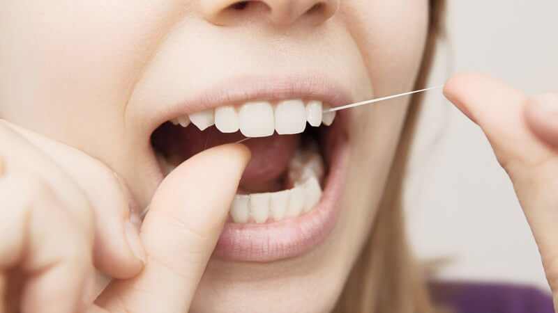 Frau reinigt die Zahnzwischenräume der Schneidezähne mit Zahnseide