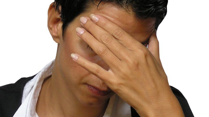 Kurzhaarige Frau hält sich linke Hand vor an Stirn vors Gesicht, Kopfschmerzen