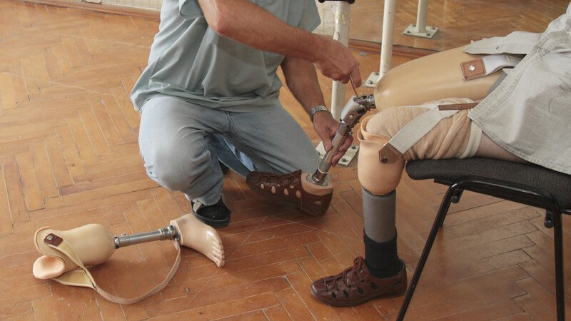 Mann sitzt auf Stuhl und bekommt eine Beinprothese angezogen