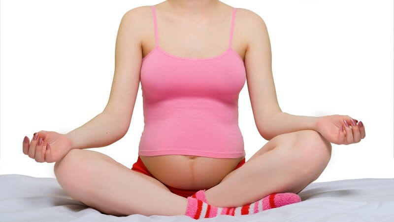 Junge schwangere Frau sitzt im Schneidersitz