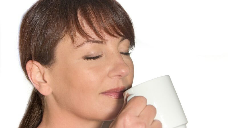 Dunkelhaarige Frau hält Kaffeebecher vor Nase und riecht den Duft mit geschlossenen Augen
