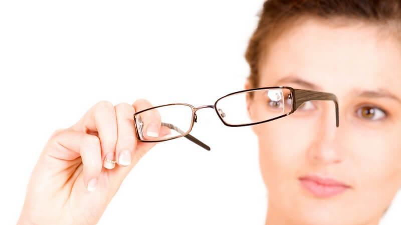Junge Frau hält Brille hoch und schaut durch die Gläser