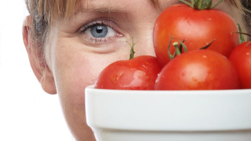 Frau hält Schüssel mit frischen Tomaten vor ihr Gesicht