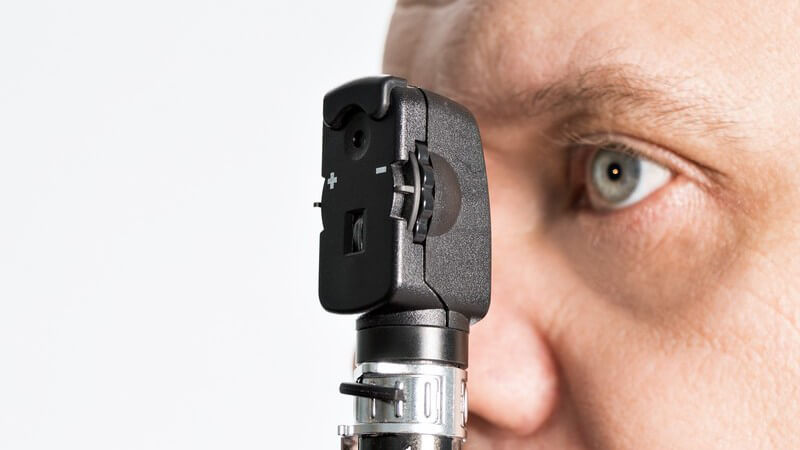 Mann guckt mit seinem linken Auge in ein kleines augenärztliches Untersuchungsgerät