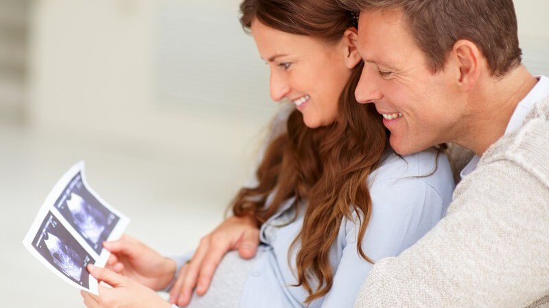 Paar schaut sich lächelnd Ultraschallbild von ihrem Baby an