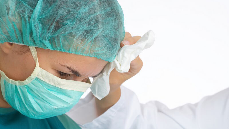 Nahaufnahme Chirurgin mit Mundschutz, sie bekommt mit Tupfer die Stirn abgetupft