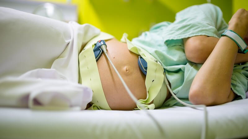 Schwangere Frau liegt im Krankenhausbett auf der Seite und ist am Wehenschreiber (CTG) angeschlossen