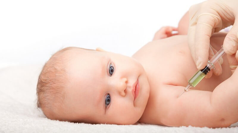 Baby liegt auf Decke und bekommt einen Impfstoff in den rechten Oberarm gespritzt