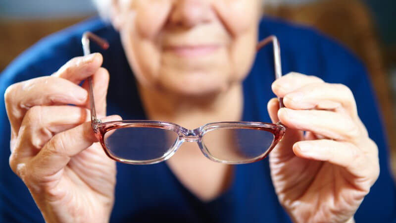 Eine Brille in den Händen einer alten Frau in blauer Kleidung