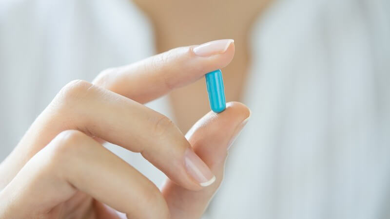 Frau hält eine blaue Kapsel-Tablette zwischen den Fingern