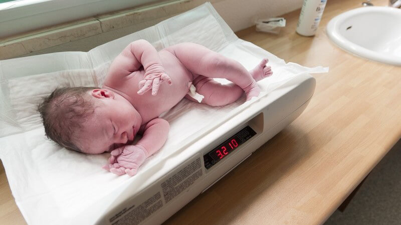 Neugeborenes liegt auf einer Waage und wiegt 3210 Gramm