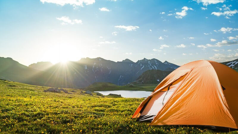 Abenteuerreisen mit Camping: Zelt in Naturlandschaft, im Hintergrund Berge und ein See