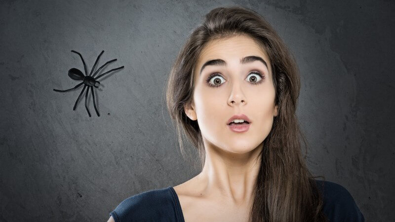 Erschrocken guckende Frau vor einem schwarzen Hintergrund, in der Ecke krabbelt eine Spinne (Fotomontage)
