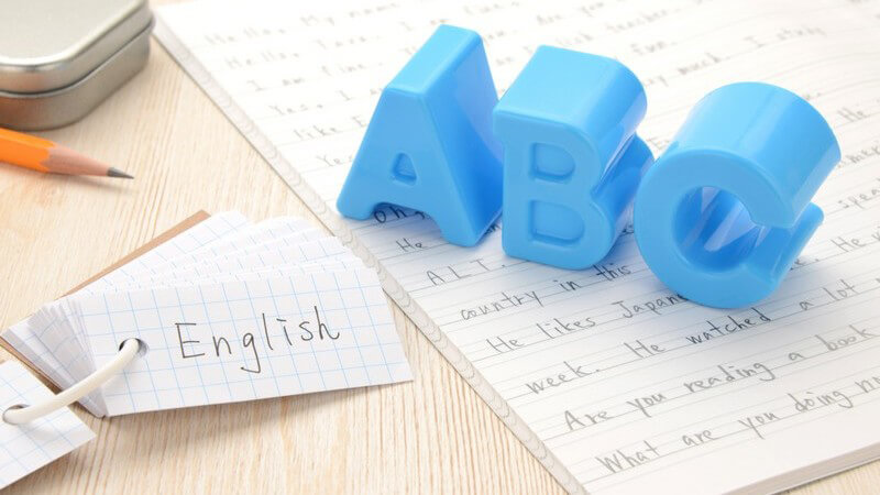 Blaue Buchstaben "ABC" stehen auf einem Schulheft, daneben Vokabelkärtchen und ein Bleistift