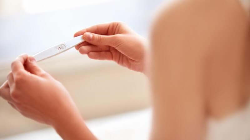 Frau hält einen weißen Schwangerschaftstest in der Hand