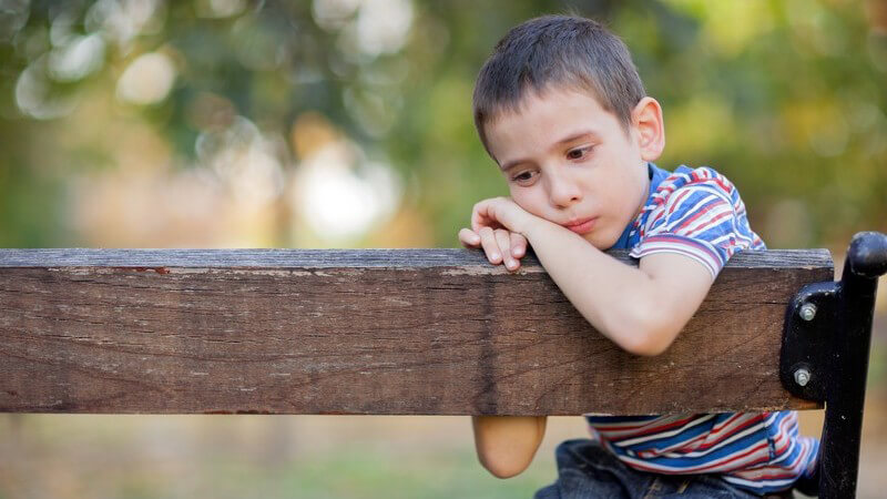 Kleiner Junge sitzt traurig auf einer Parkbank