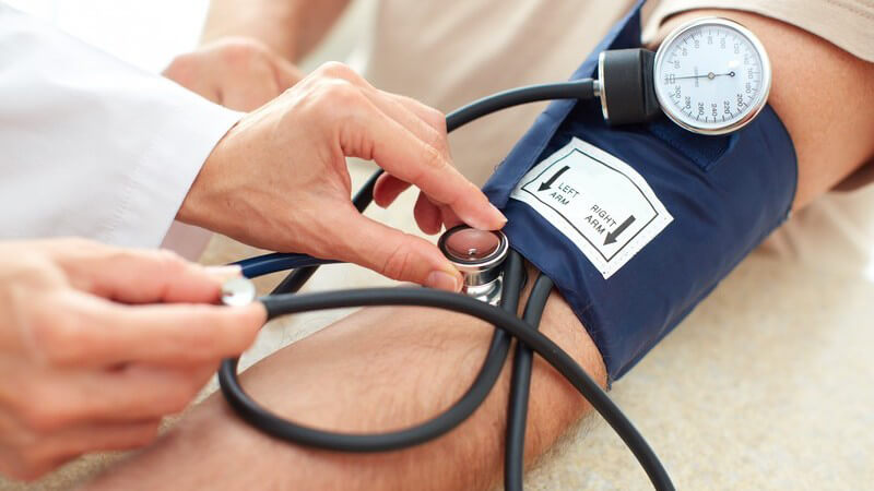 Arzt misst den Blutdruck am linken Arm eines Patienten, blaue Manschette