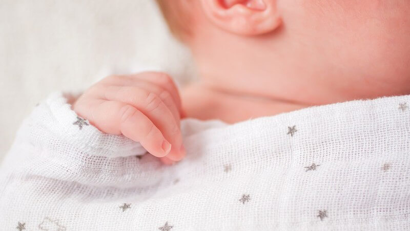 Nahaufnahme der Hand eines Säuglings, zugedeckt mit weißem Tuch mit grauen Sternchen