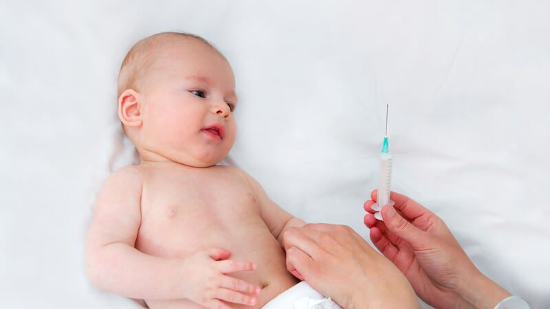 Baby in Windel auf weißer Decke bekommt eine Spritze zur Schutzimpfung